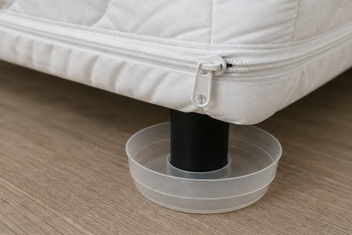 Mattress encasement zipper and interceptor cup installed beneath a bed leg